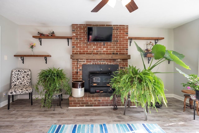 living area featuring a wood stove, a ceiling fan, baseboards, and wood finished floors