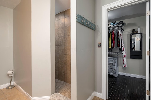 bathroom featuring a spacious closet, tiled shower, and baseboards