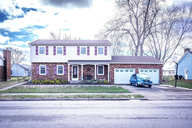 colonial-style house with aphalt driveway, a front yard, brick siding, and a garage