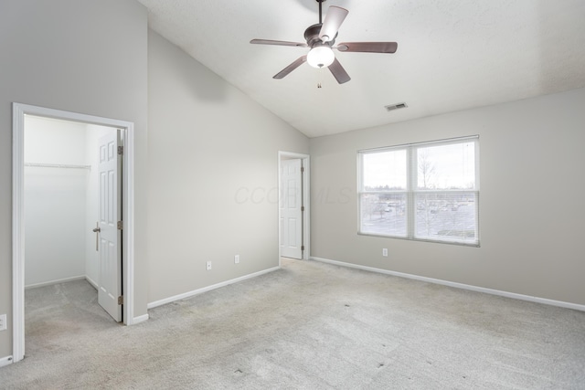 unfurnished bedroom featuring lofted ceiling, a walk in closet, light carpet, a closet, and ceiling fan