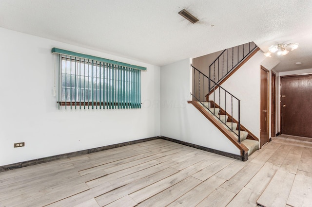 empty room featuring a chandelier, a textured ceiling, and light wood-type flooring