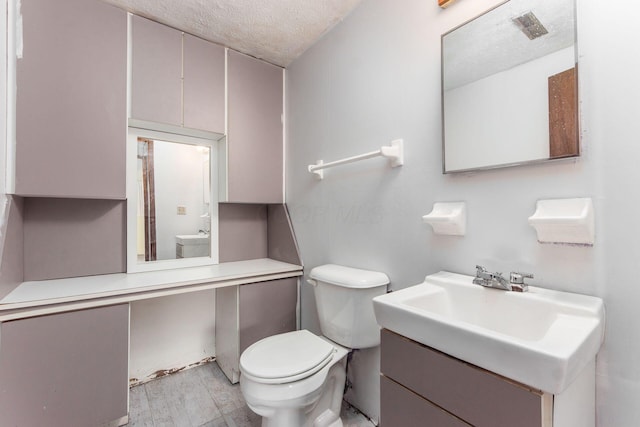 bathroom featuring vanity, hardwood / wood-style floors, a textured ceiling, and toilet