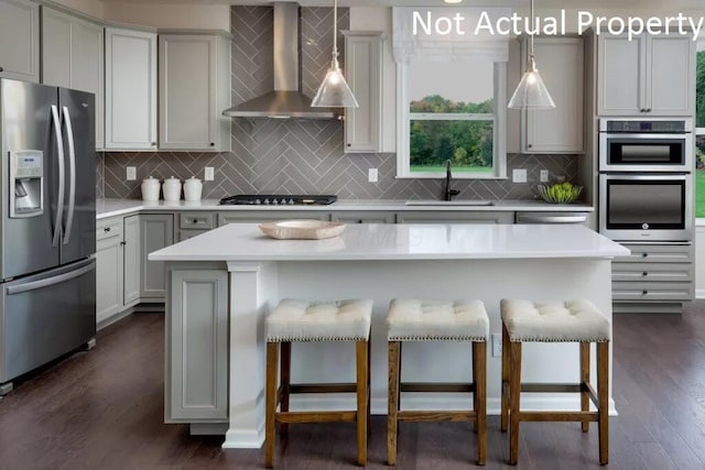 kitchen with a kitchen bar, sink, a center island, appliances with stainless steel finishes, and wall chimney range hood