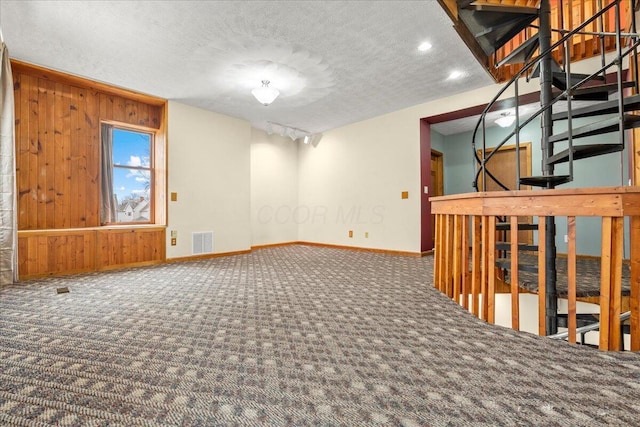 carpeted empty room featuring wooden walls and a textured ceiling