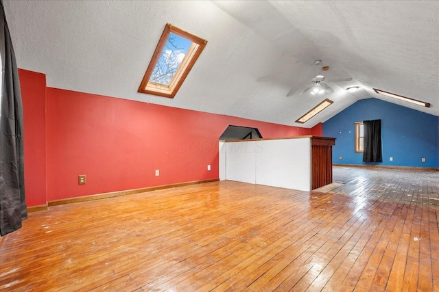 bonus room featuring hardwood / wood-style flooring, ceiling fan, lofted ceiling with skylight, and a textured ceiling