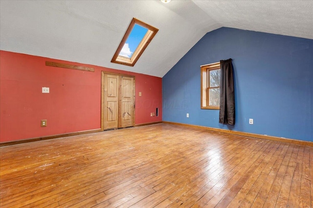 additional living space featuring vaulted ceiling with skylight, a textured ceiling, and light hardwood / wood-style flooring