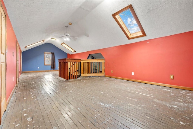 additional living space featuring ceiling fan, lofted ceiling with skylight, hardwood / wood-style floors, and a textured ceiling