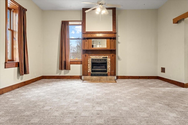 unfurnished living room with ceiling fan, light colored carpet, and a tile fireplace