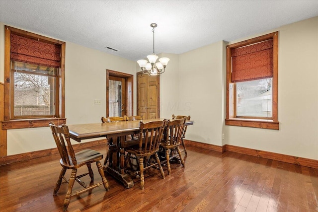 dining space with wood-type flooring, a notable chandelier, and a textured ceiling