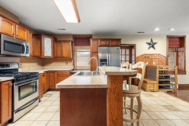 kitchen featuring light tile patterned flooring, sink, a center island with sink, a kitchen breakfast bar, and stainless steel appliances