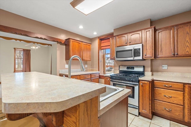 kitchen with light tile patterned floors, a breakfast bar area, ceiling fan, appliances with stainless steel finishes, and a center island