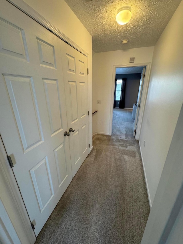 corridor featuring a textured ceiling and dark colored carpet