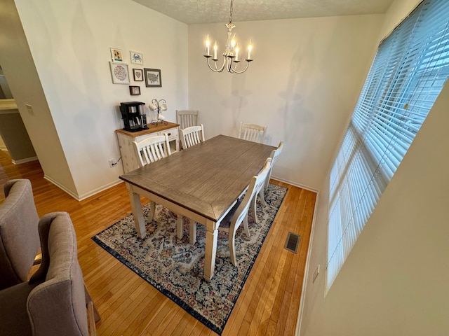 dining area featuring an inviting chandelier, light hardwood / wood-style flooring, and a textured ceiling