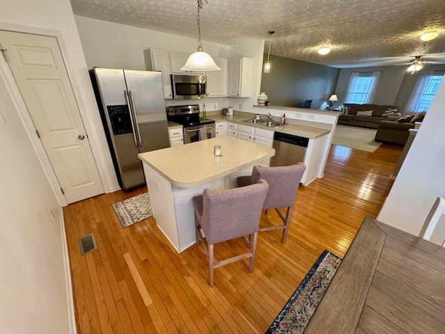 kitchen featuring appliances with stainless steel finishes, sink, a breakfast bar area, white cabinets, and hanging light fixtures