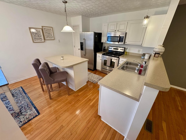 kitchen with a breakfast bar area, white cabinetry, hanging light fixtures, stainless steel appliances, and light hardwood / wood-style floors