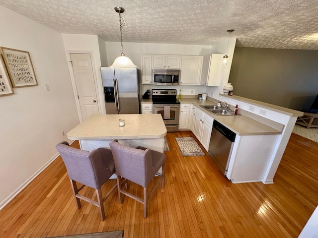 kitchen featuring appliances with stainless steel finishes, decorative light fixtures, sink, white cabinets, and light hardwood / wood-style flooring