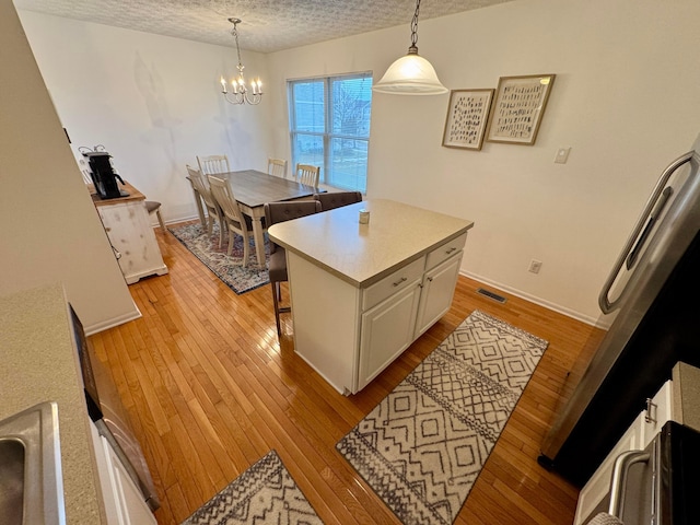 kitchen with white cabinetry, hanging light fixtures, a center island, and light wood-type flooring