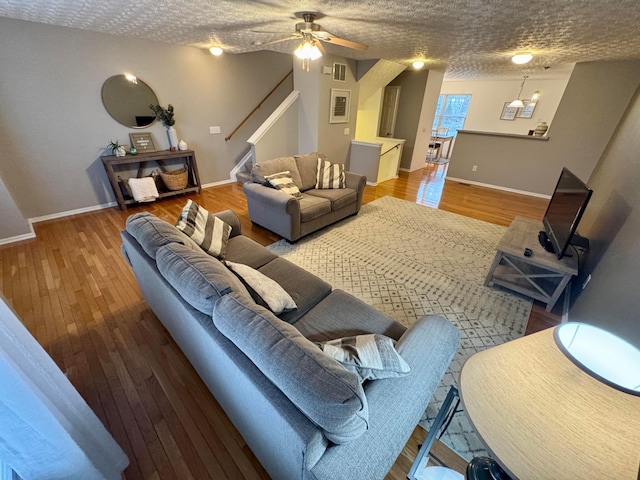 living room with wood-type flooring, ceiling fan with notable chandelier, and a textured ceiling