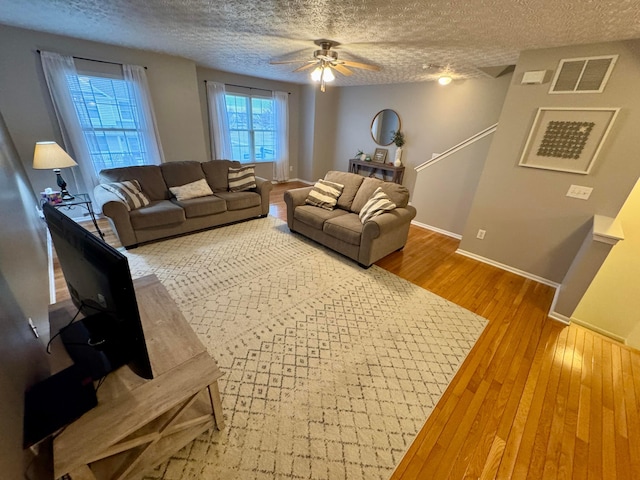 living room featuring hardwood / wood-style flooring, ceiling fan, and a textured ceiling