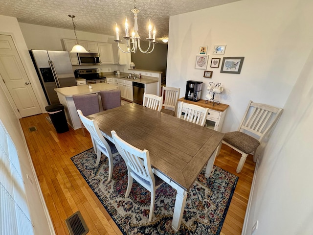 dining room featuring an inviting chandelier, sink, light hardwood / wood-style floors, and a textured ceiling