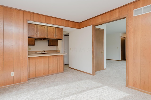 kitchen with sink, crown molding, wooden walls, kitchen peninsula, and light colored carpet