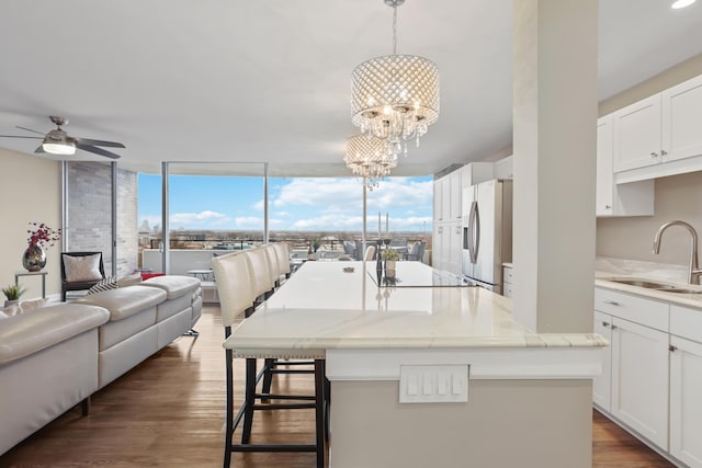 kitchen featuring sink, white cabinetry, stainless steel refrigerator with ice dispenser, an island with sink, and decorative light fixtures