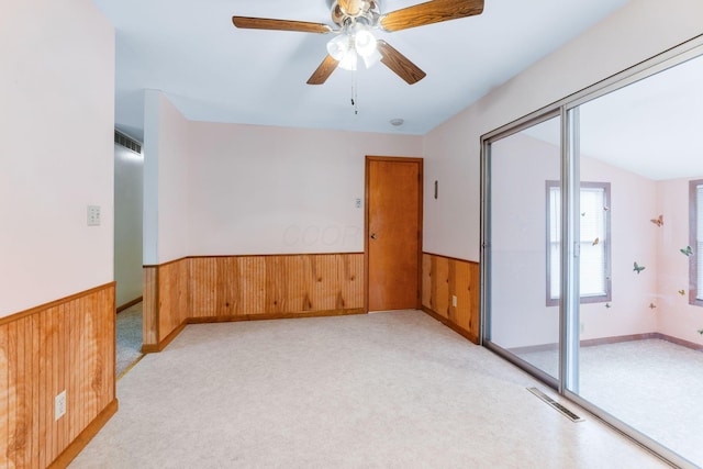 carpeted spare room with wooden walls and ceiling fan