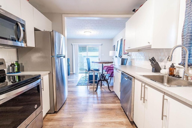 kitchen with sink, light hardwood / wood-style flooring, appliances with stainless steel finishes, tasteful backsplash, and white cabinets