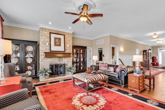 living room featuring hardwood / wood-style flooring, ceiling fan, ornamental molding, and a fireplace