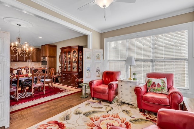 living room with hardwood / wood-style flooring, crown molding, and ceiling fan with notable chandelier