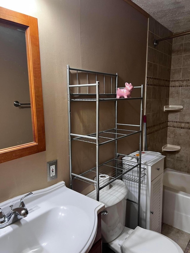 full bathroom with sink, a textured ceiling, tiled shower / bath, and toilet