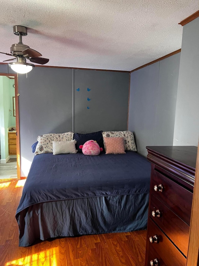 bedroom featuring ceiling fan, wood-type flooring, ornamental molding, and a textured ceiling