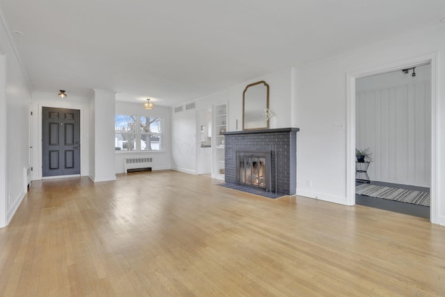 unfurnished living room with built in features, radiator heating unit, a fireplace, ornamental molding, and light wood-type flooring