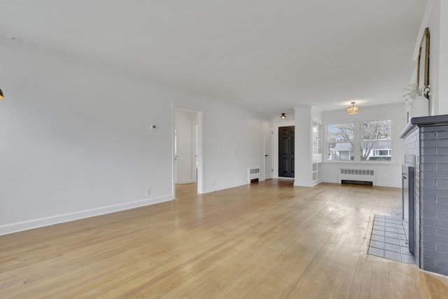 unfurnished living room with radiator heating unit, light hardwood / wood-style floors, and a brick fireplace