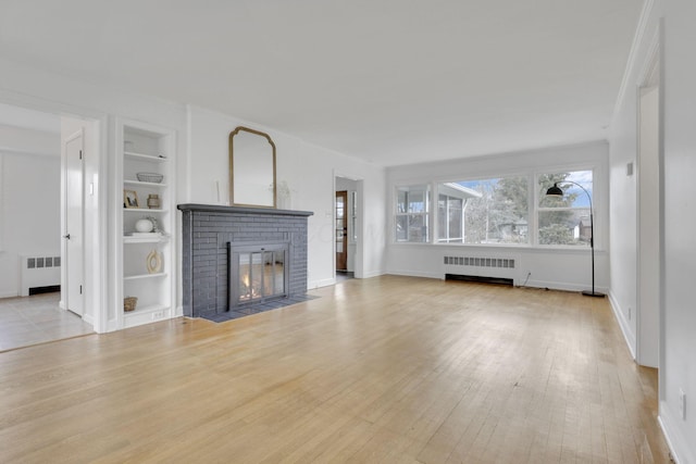 unfurnished living room with built in shelves, a fireplace, radiator, and light hardwood / wood-style flooring