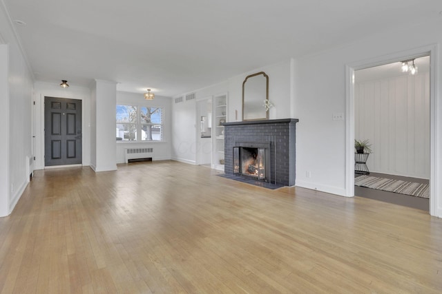 unfurnished living room with radiator heating unit, a fireplace, built in features, and light wood-type flooring