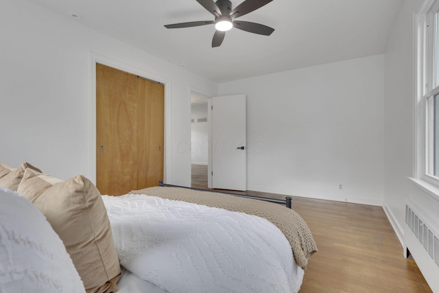 bedroom featuring radiator heating unit, multiple windows, ceiling fan, light wood-type flooring, and a closet