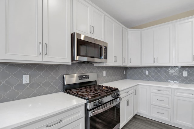 kitchen featuring dark wood-type flooring, appliances with stainless steel finishes, white cabinetry, backsplash, and light stone countertops