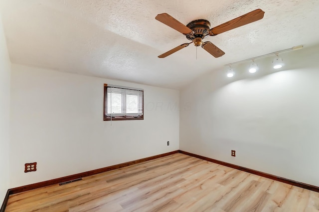 empty room featuring ceiling fan, track lighting, light hardwood / wood-style floors, and a textured ceiling