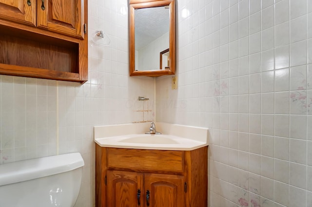 bathroom featuring vanity, toilet, tile walls, and a textured ceiling