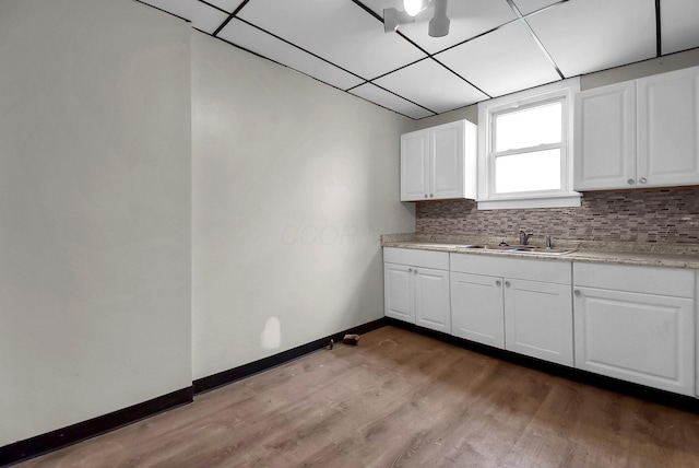 kitchen with tasteful backsplash, sink, white cabinets, and light hardwood / wood-style flooring