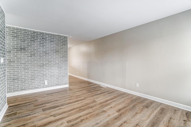 unfurnished room featuring light hardwood / wood-style flooring and brick wall