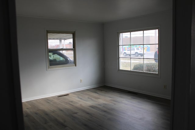 empty room with wood finished floors, visible vents, and baseboards