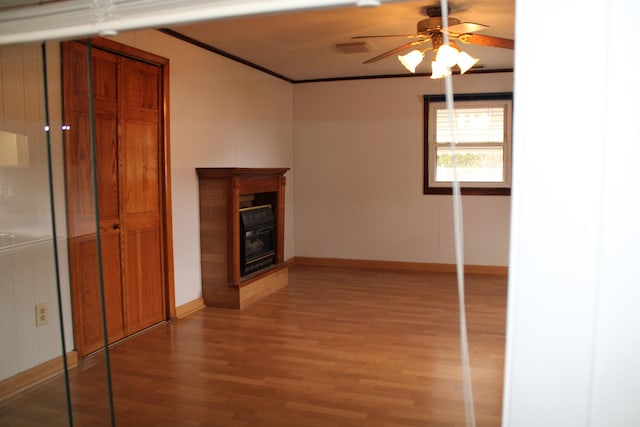 unfurnished living room featuring a ceiling fan, baseboards, light wood-type flooring, a glass covered fireplace, and crown molding