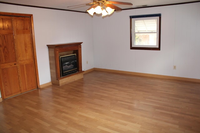 unfurnished living room featuring a ceiling fan, baseboards, light wood finished floors, a glass covered fireplace, and crown molding