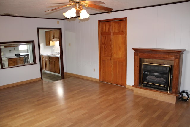 unfurnished living room with crown molding, a glass covered fireplace, a sink, and wood finished floors