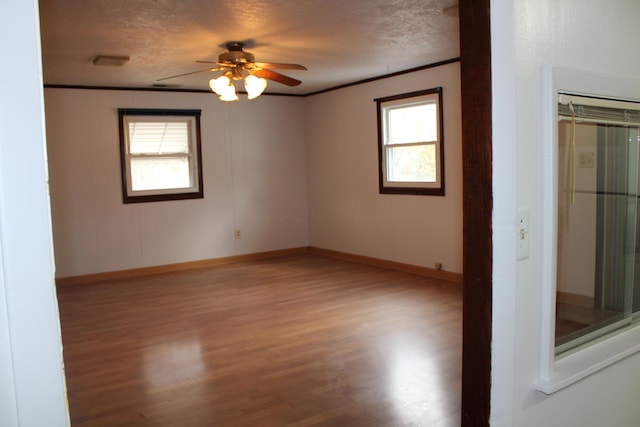 empty room featuring a textured ceiling, ornamental molding, plenty of natural light, and wood finished floors