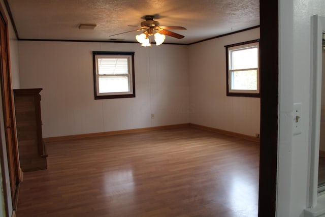 empty room with ornamental molding, ceiling fan, a textured ceiling, wood finished floors, and baseboards