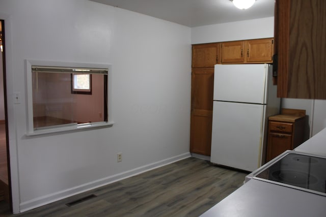 kitchen with dark wood-style floors, brown cabinets, visible vents, freestanding refrigerator, and baseboards