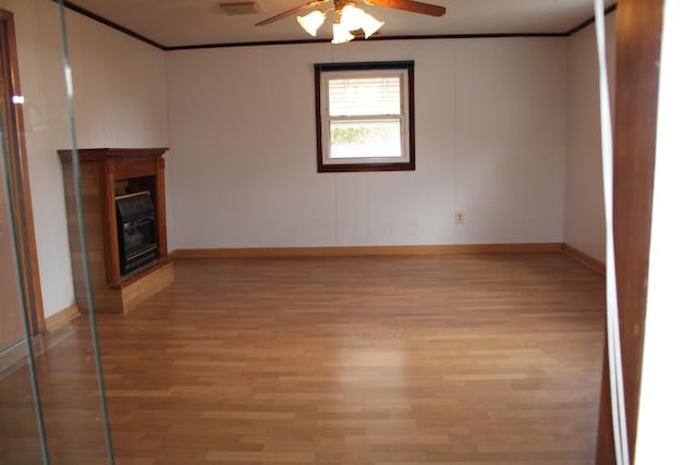 unfurnished living room with ornamental molding, a glass covered fireplace, a ceiling fan, light wood-type flooring, and baseboards